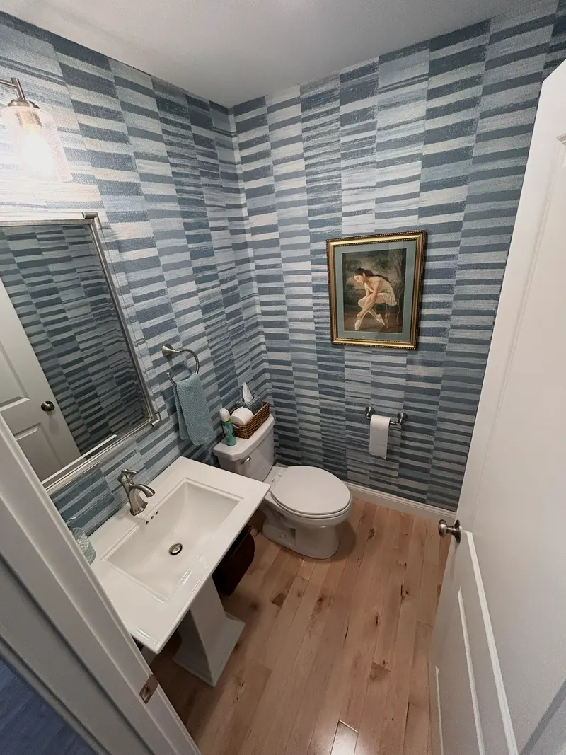 Powder room with patterned blue wallpaper, a pedestal sink and hardwood floor