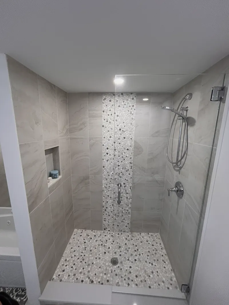 Tiled shower with large-format marble-look tile and a pebble mosaic floor and accent band