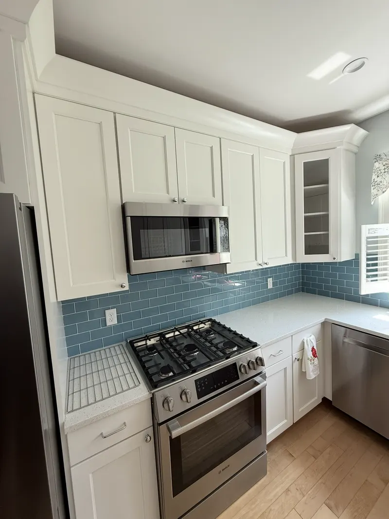 Kitchen with white shaker cabinets, quartz counters and a blue glass tile backsplash